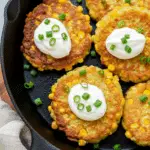 Golden corn fritters with crispy coating showing corn kernels and sour cream