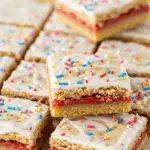 Pop Tart cookie bars with white icing, rainbow sprinkles, and visible strawberry filling layers