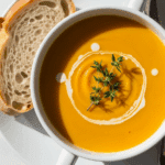 Butternut squash soup in white bowl with cream swirl and thyme garnish