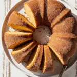 Apple cider doughnut cake sliced on plate showing golden interior and cinnamon coating