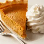 Plated pumpkin pie slice with whipped cream and fork on ceramic plate